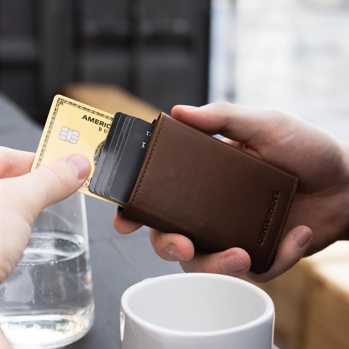 G004-cardholder-darkbrown;;Cards being pushed out of the Cardholder in dark brown, a cup in the background;;;en